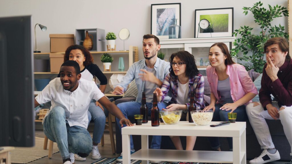 A diverse group of friends excitedly watching TV together in a modern living room setting.